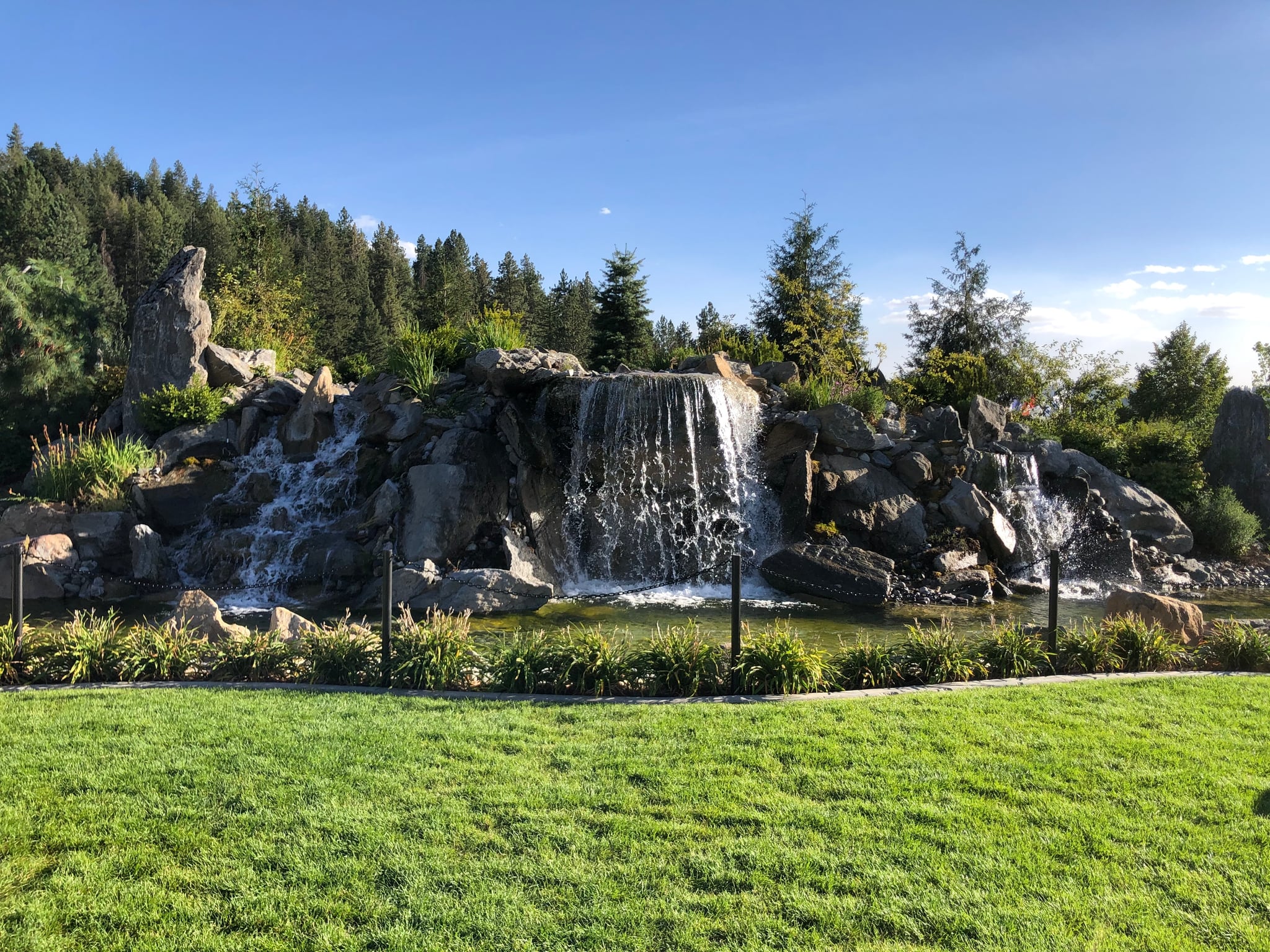Rock waterfall feature surrounded by pine trees and green lawn in Northern Idaho