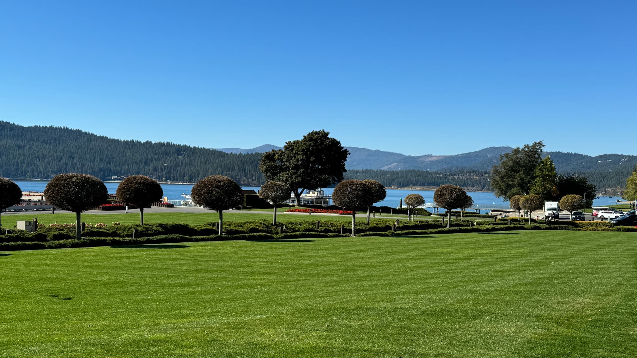 Manicured park grounds with trimmed trees overlooking a Northern Idaho lake and surrounding mountains